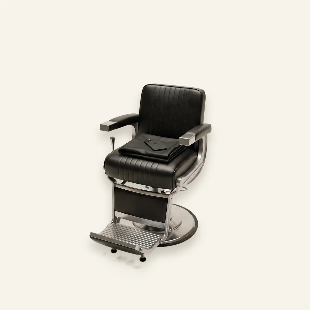 An empty barber chair with the cape folded and a phone face-down on the seat